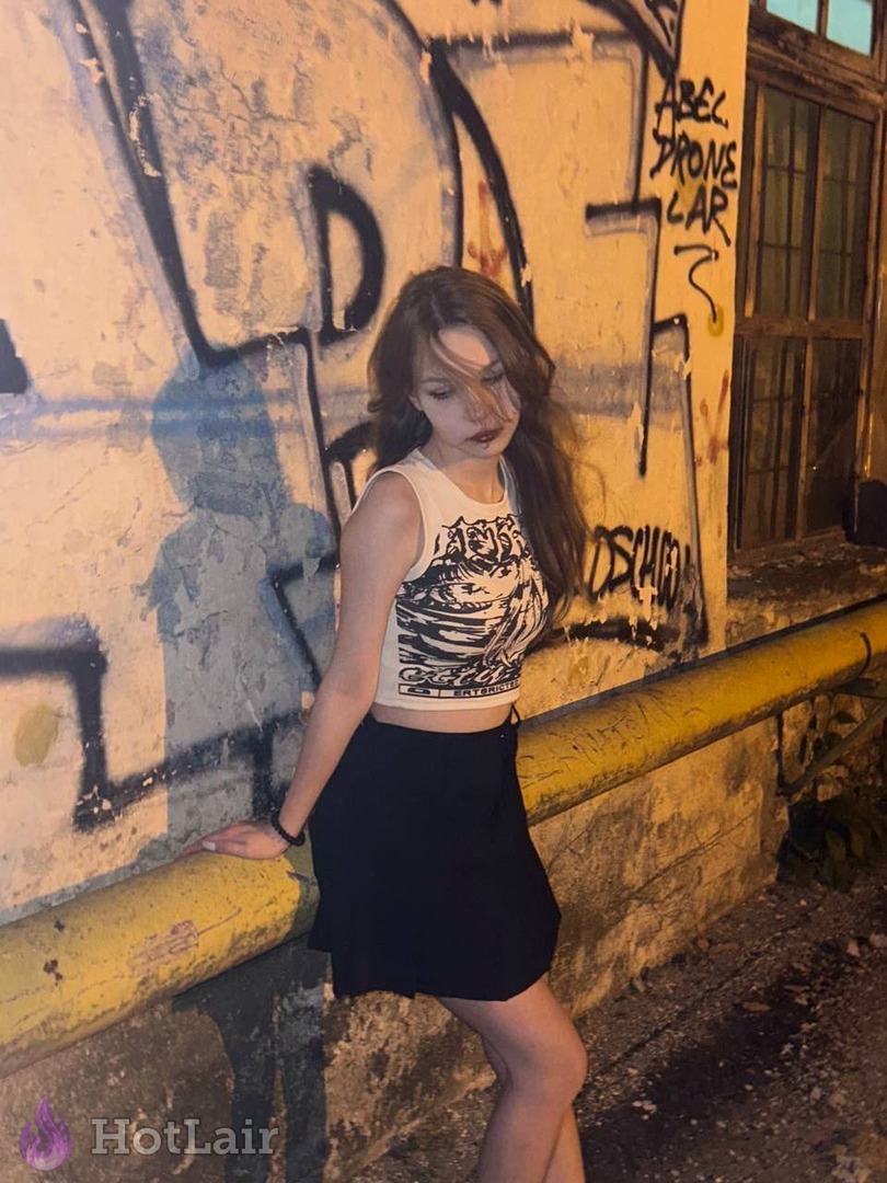 mujer en crop top gráfico y falda corta negra posando junto a pared de grafitis