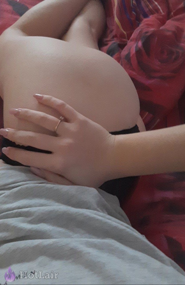 Primer plano de la nalga desnuda de una sobre la cama con sábanas rojas, mano con anillos descansando sobre ella