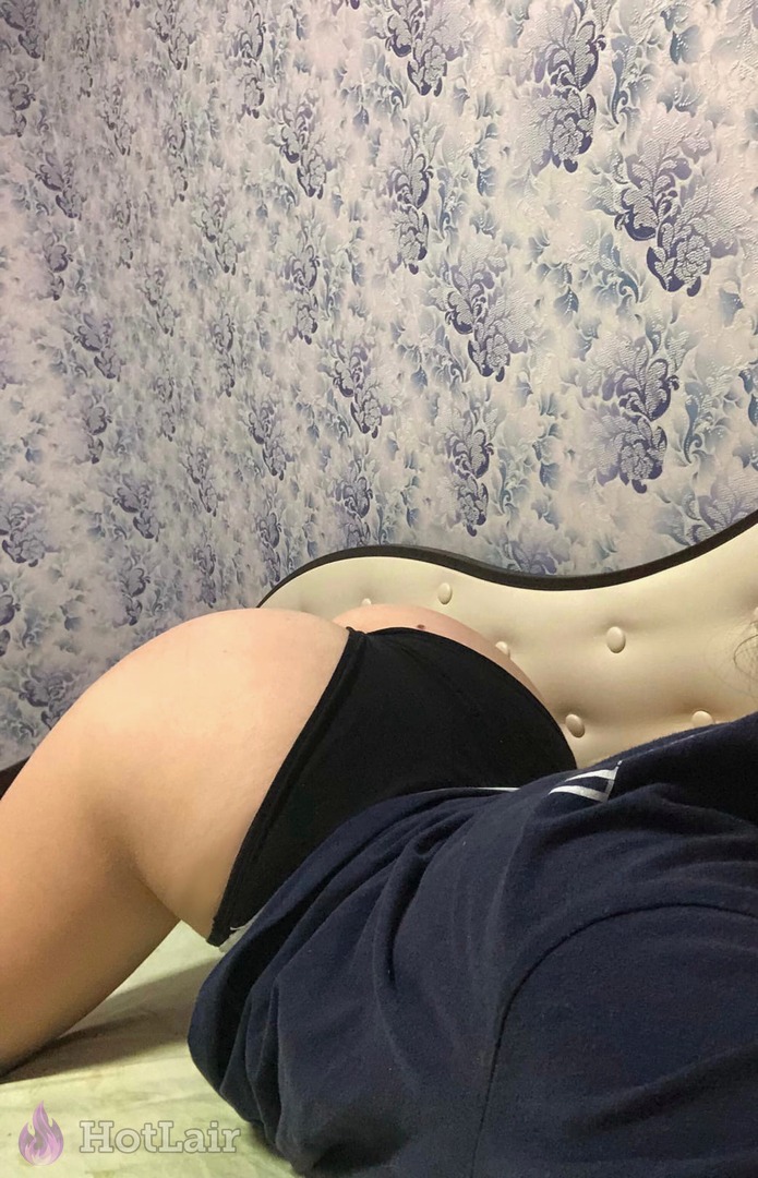 acostada en la cama con bragas negras y camiseta azul, vista lateral de sus caderas