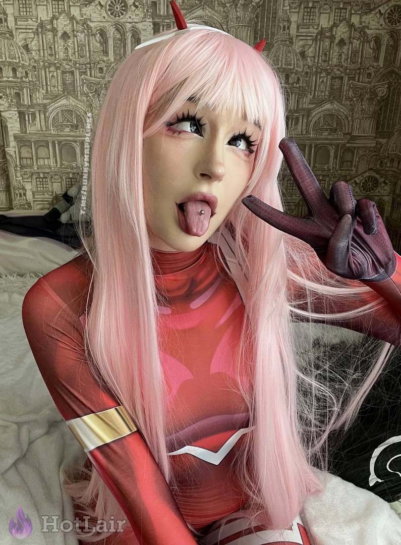 Mujer con peluca rosa y body de cosplay rojo haciendo signo de paz con la lengua afuera