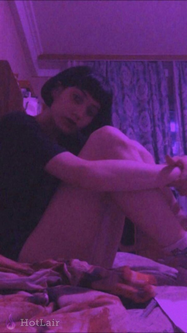 Mujer con corte bob negro corto sentada desnuda en la cama con luz púrpura