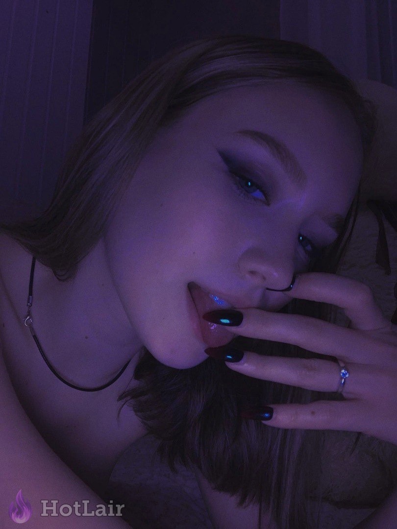 Primer plano de con piercing en la nariz bajo luz púrpura, dedo tocando los labios
