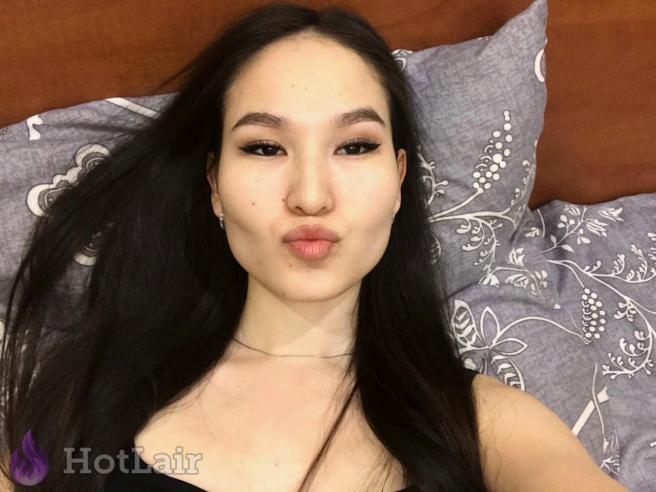 mujer con cabello largo oscuro acostada en la cama haciendo selfie con cara de beso