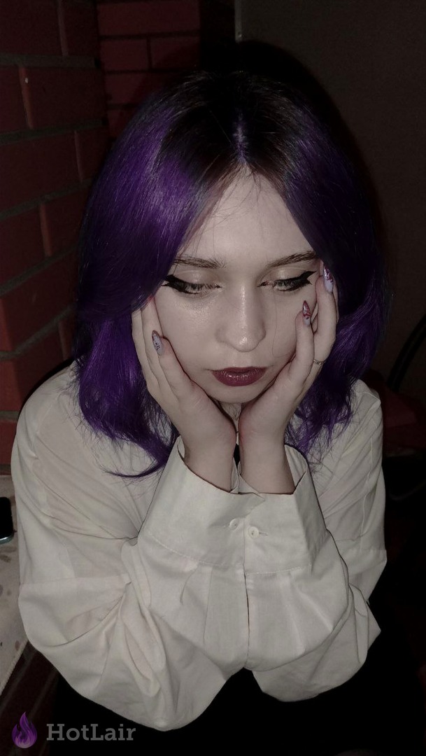 mujer con cabello morado vibrante apoyando la cara en las manos, con camisa blanca