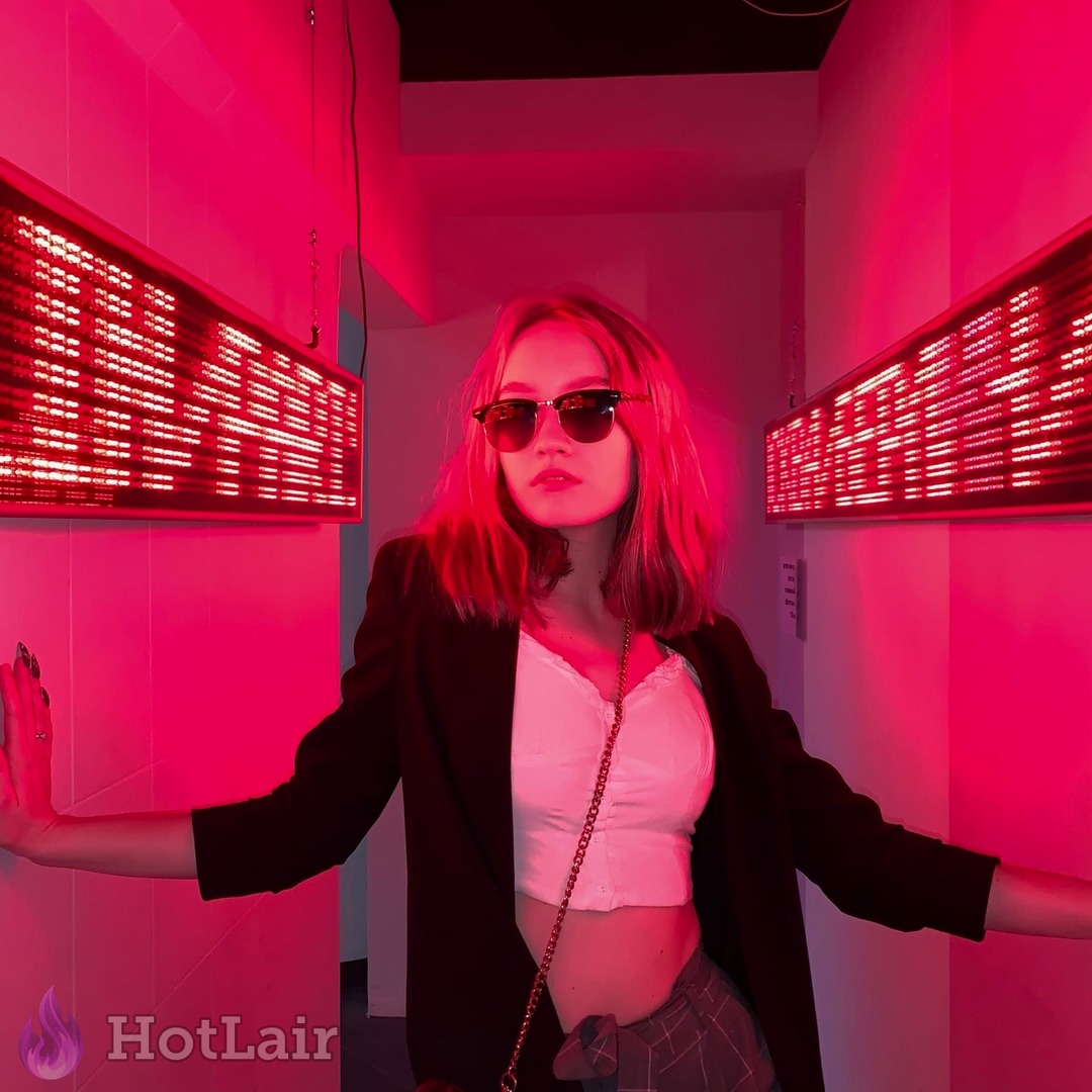 estilosa con gafas de sol y blazer negro posando en pasillo con luz neón rosa