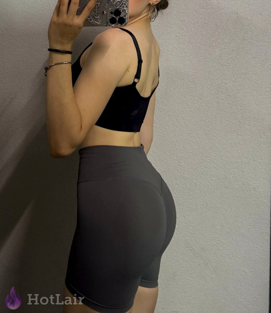 Femme athlétique en brassière noire et short gris prenant un selfie miroir de côté
