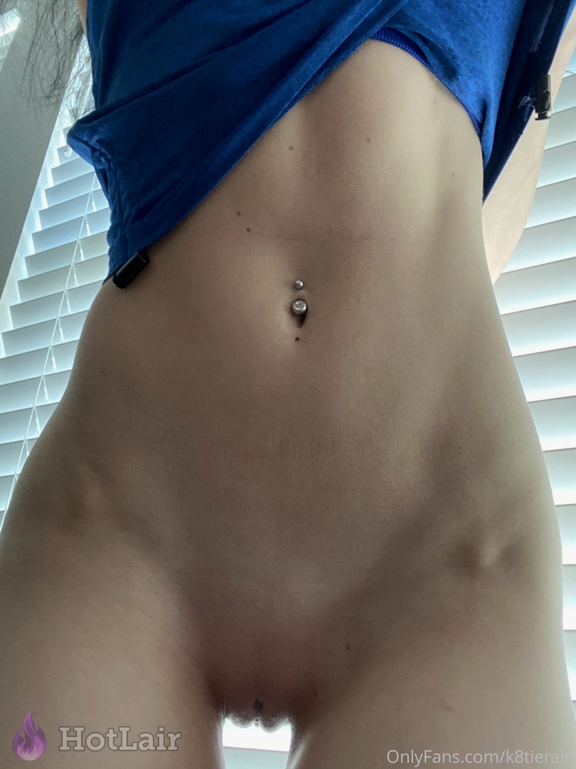 Close-up do abdômen tonificado da morena com piercing no umbigo sob camisa azul levantada