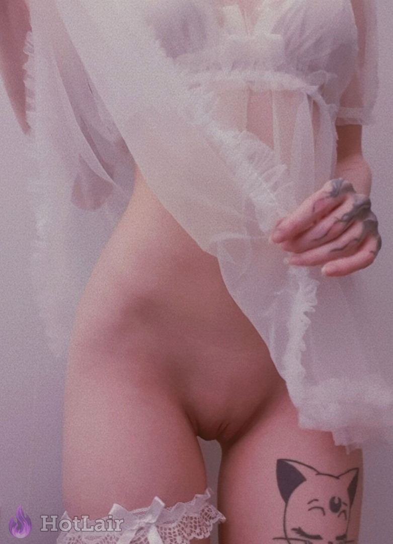 Mujer en doll blanco transparente con volantes y liguero, mano tatuada en la cadera, tatuaje de gato en el muslo