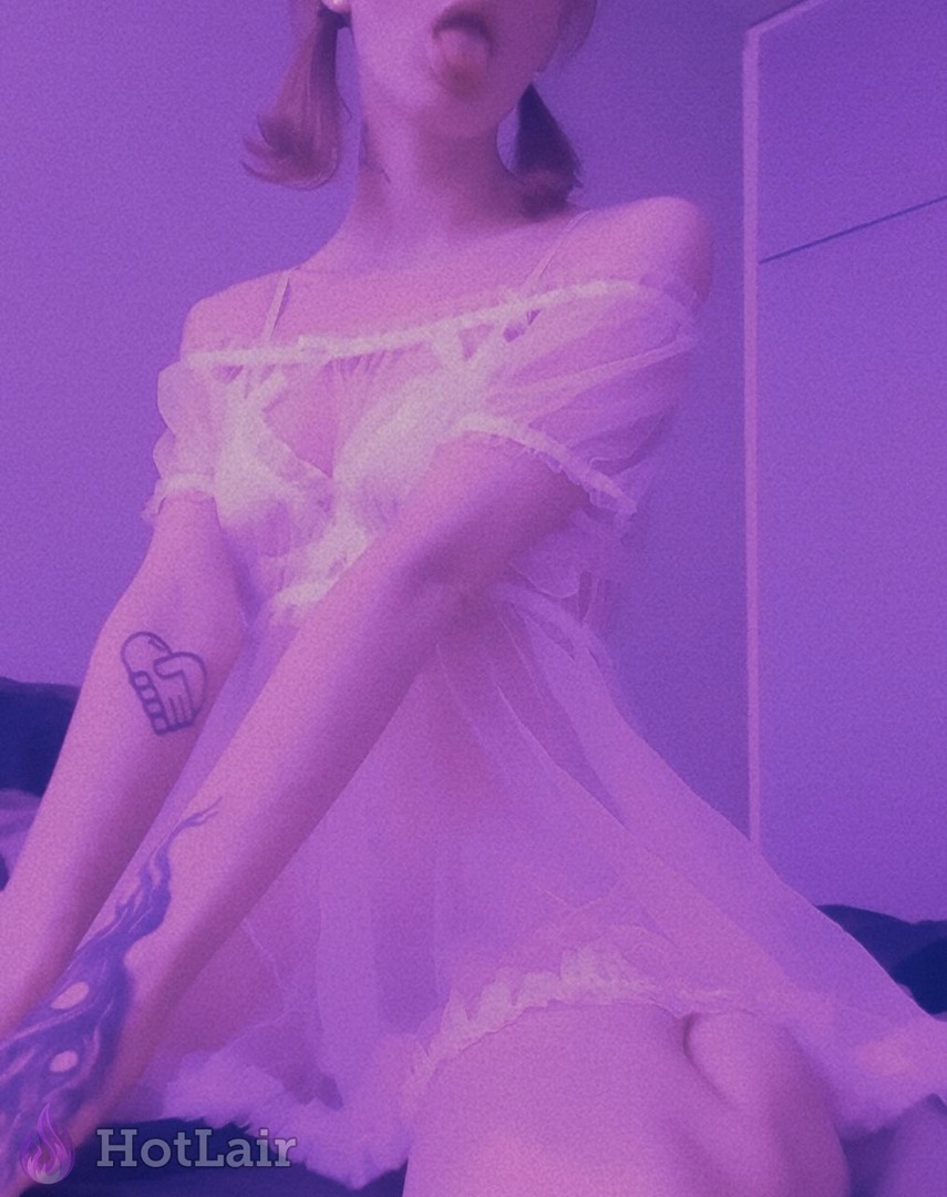 en vestido de lencería blanco transparente con hombros descubiertos y coletas, sacando la lengua, tatuajes visibles