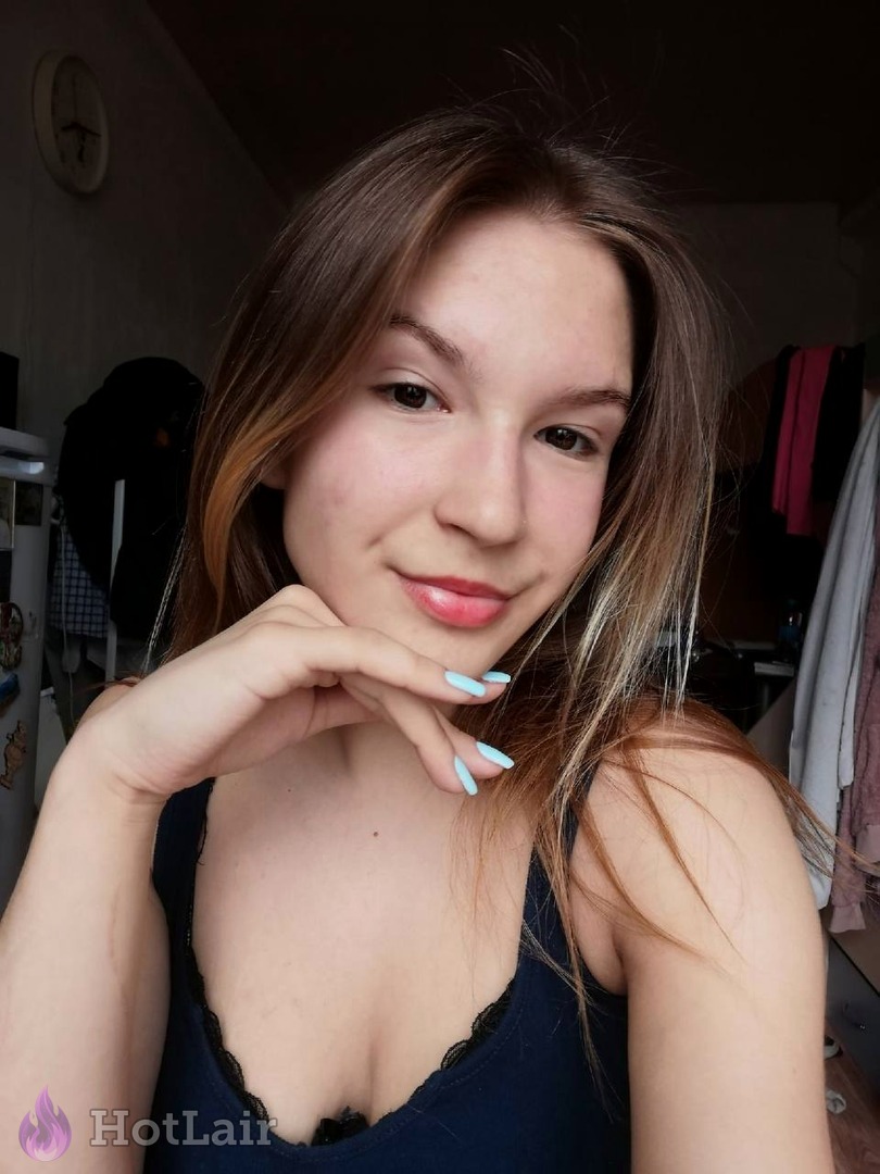Portrait rapproché souriant d’une jeune femme aux cheveux châtain clair et ongles bleu clair, main sous le menton