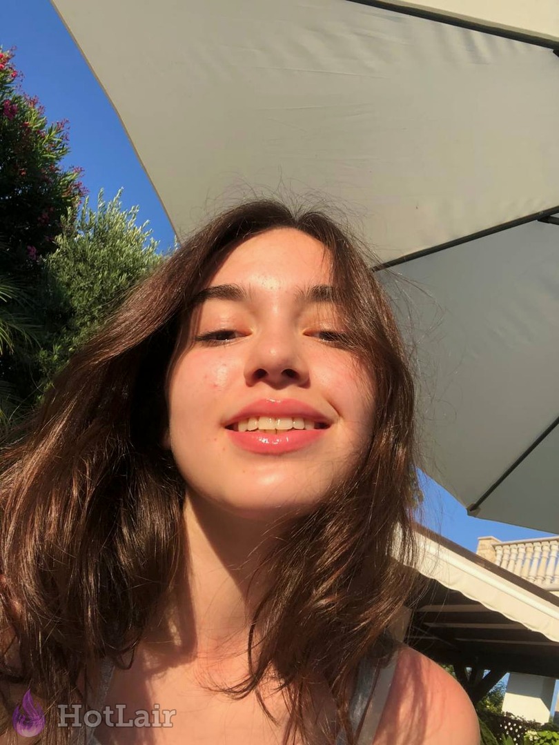 Portrait rapproché souriant d’une jeune femme aux longs cheveux châtains en extérieur sous parasol blanc par jour ensoleillé