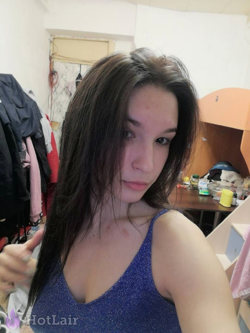 Selfie d’une jeune femme aux longs cheveux noirs en top bleu brillant faisant un pouce en l’air