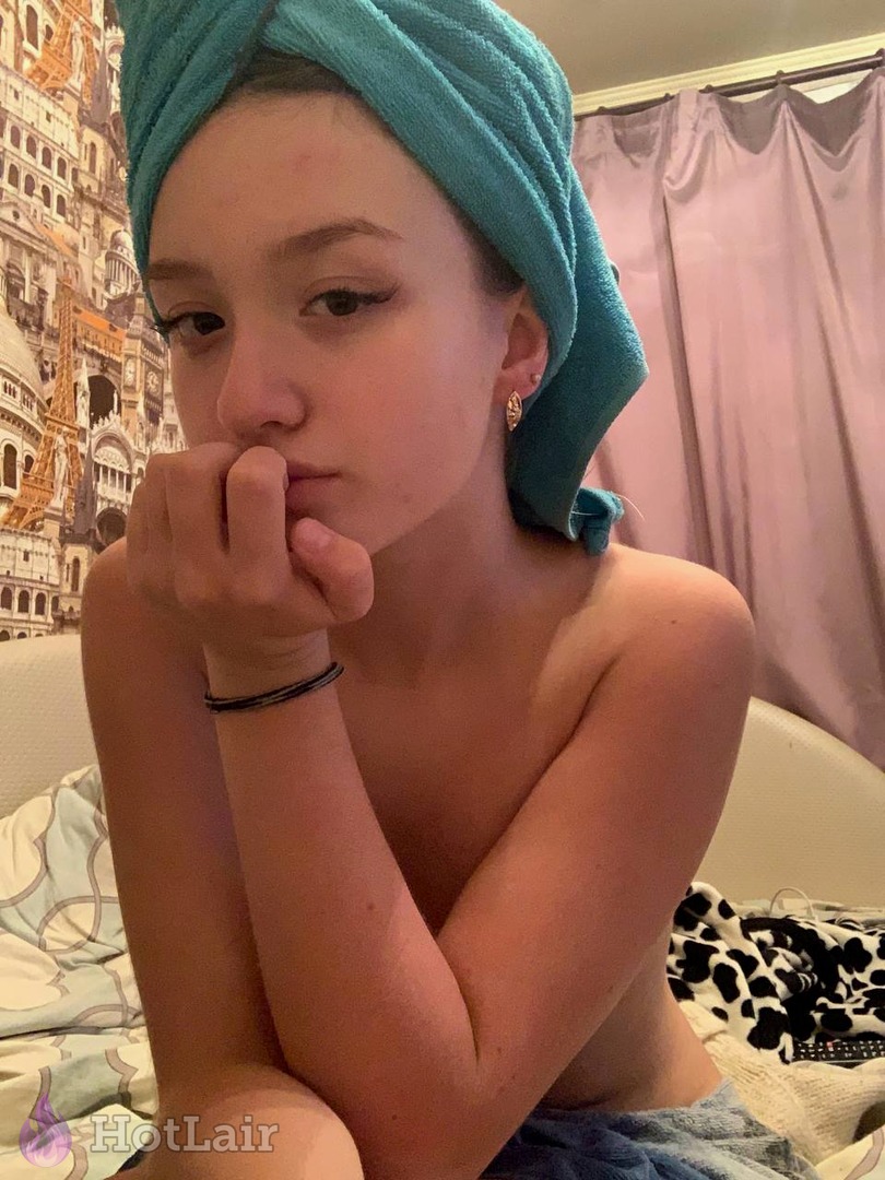 Chica topless con toalla en la cabeza posando pensativa en la cama