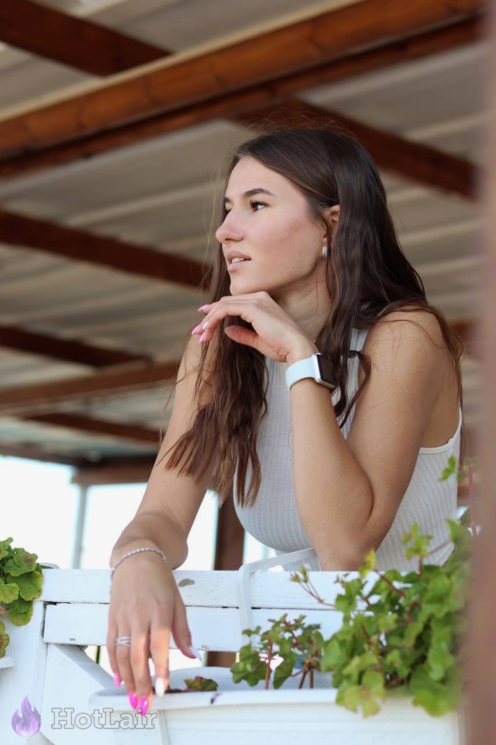 Belle jeune femme aux longs cheveux bruns posant sur un balcon avec vue sur la mer