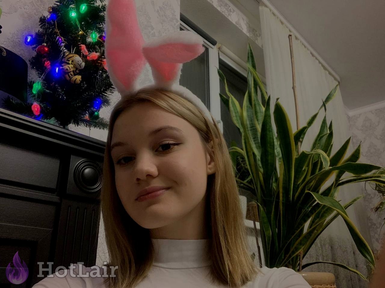 rubia con diadema de orejas de conejo rosa delante de un árbol de Navidad
