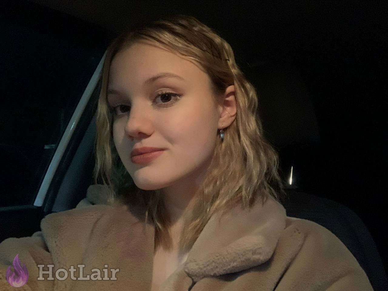 rubia en abrigo de peluche beige haciéndose un selfie dentro de un coche por la noche