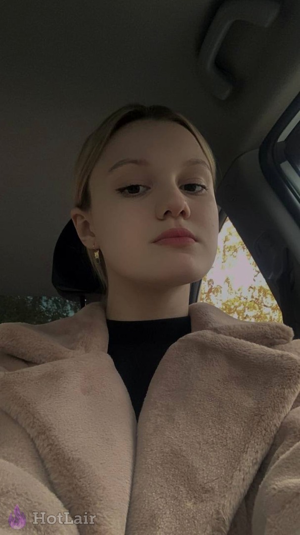 en abrigo de peluche beige haciéndose un selfie dentro de un coche