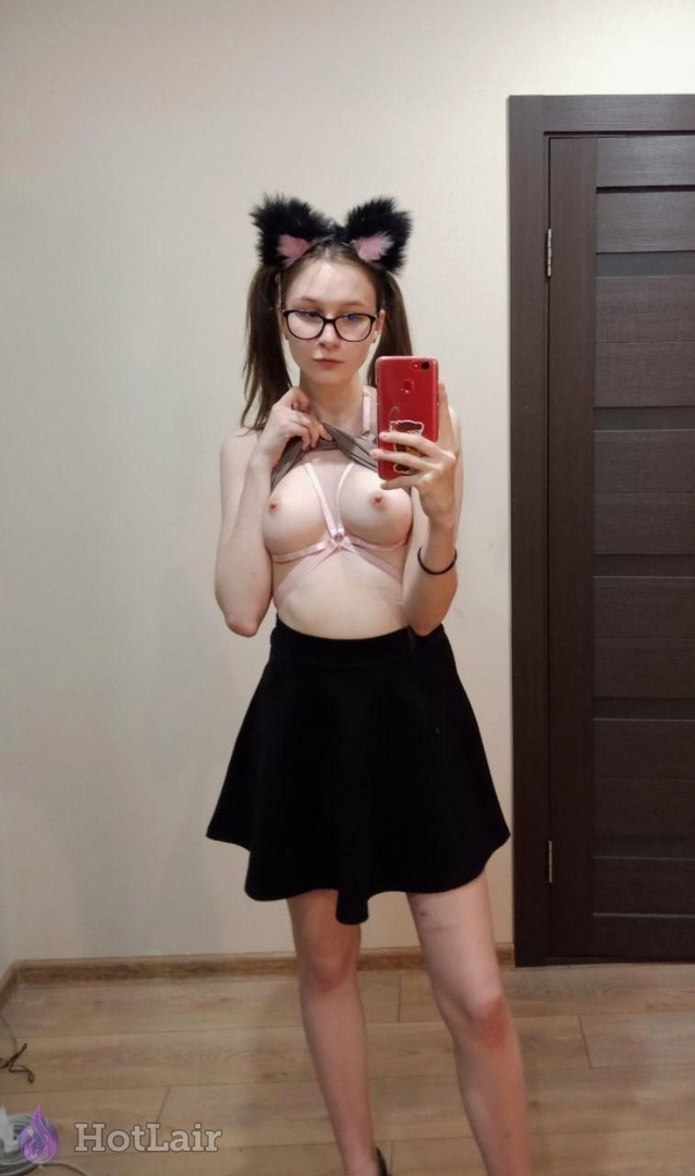 Garota com tiara de orelhas de gato e óculos tirando selfie no espelho de sutiã rosa arnês e saia preta