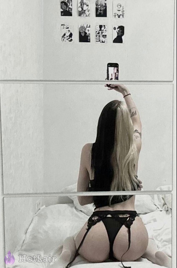 Mujer de cabello bicolor negro y rubio en lencería negra haciéndose selfie en espejo desde atrás
