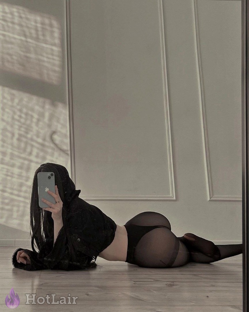 Mujer en chaqueta negra y medias transparentes negras tumbada en el suelo haciéndose selfie en espejo, foco en culo