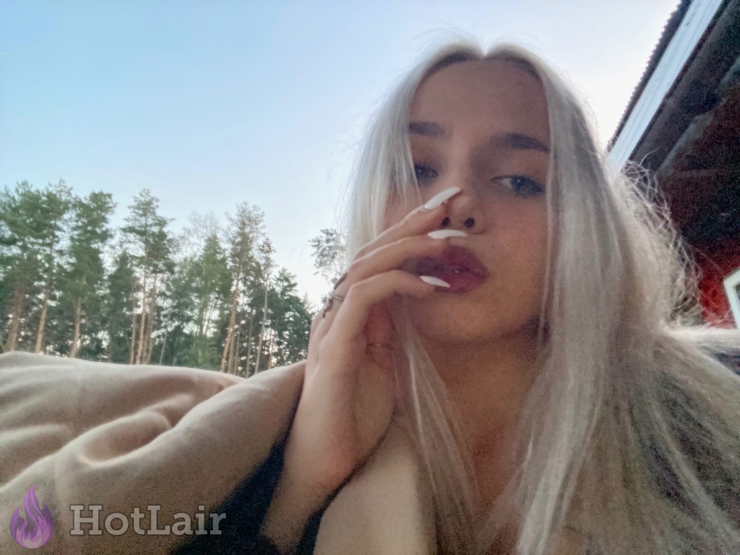 Rubia platino haciéndose selfie al aire libre envuelta en manta, mano cerca de la cara