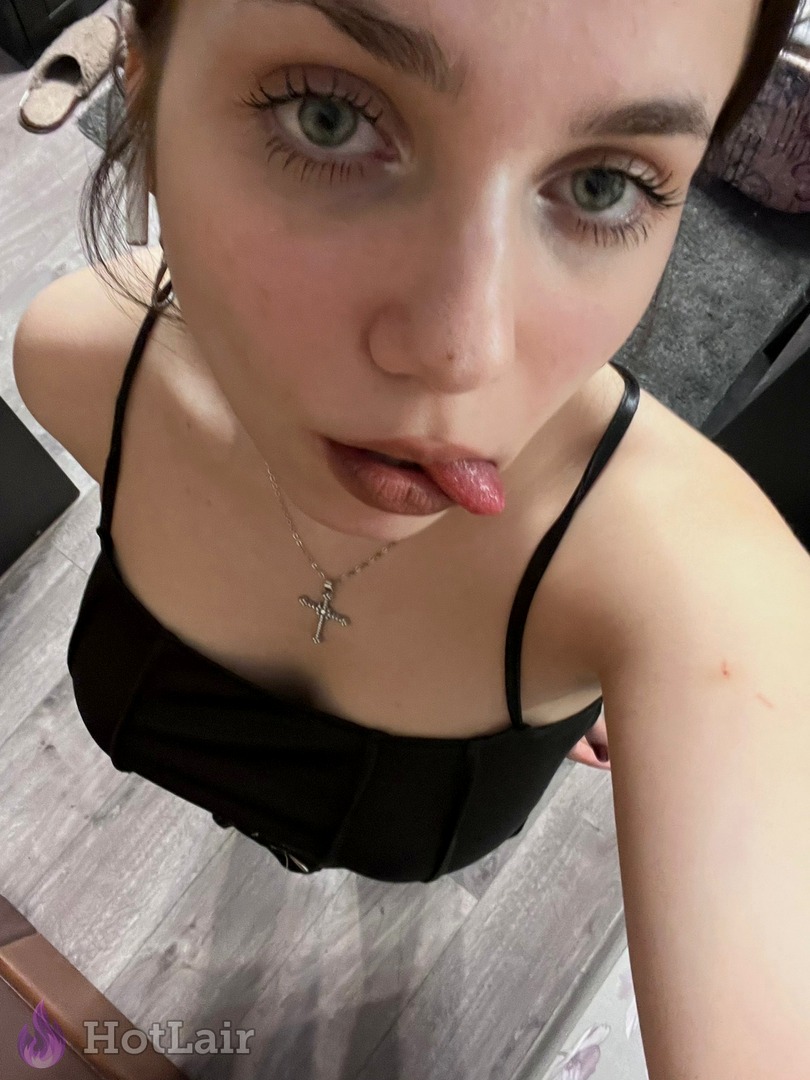 Selfie close-up de chica con ojos verdes y collar de cruz sacando la lengua