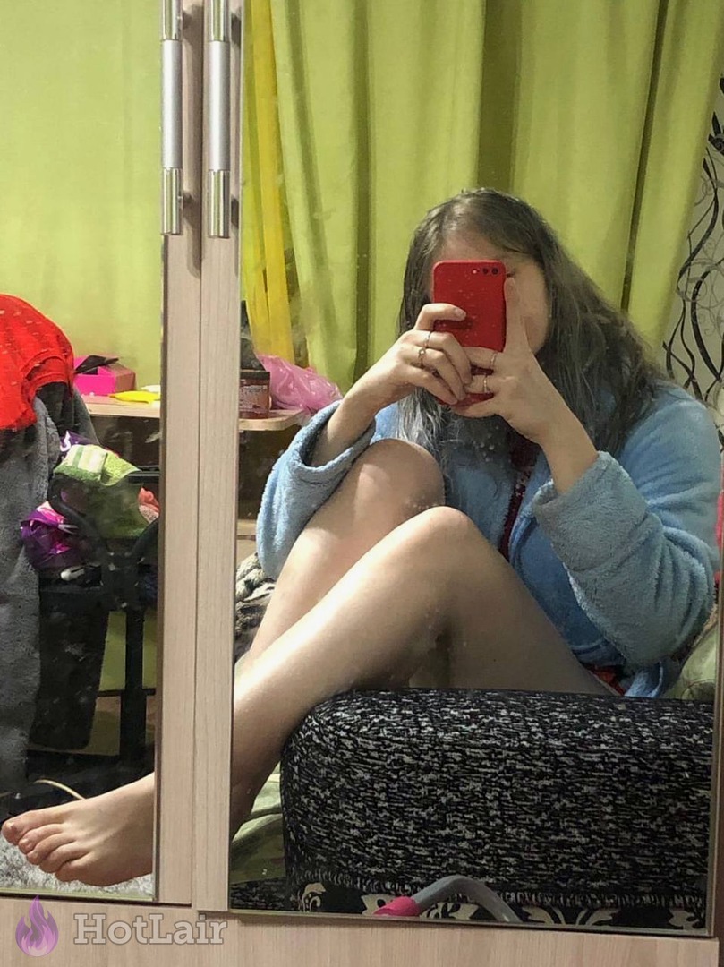 en bata azul sentada en taburete haciéndose selfie en espejo, piernas cruzadas