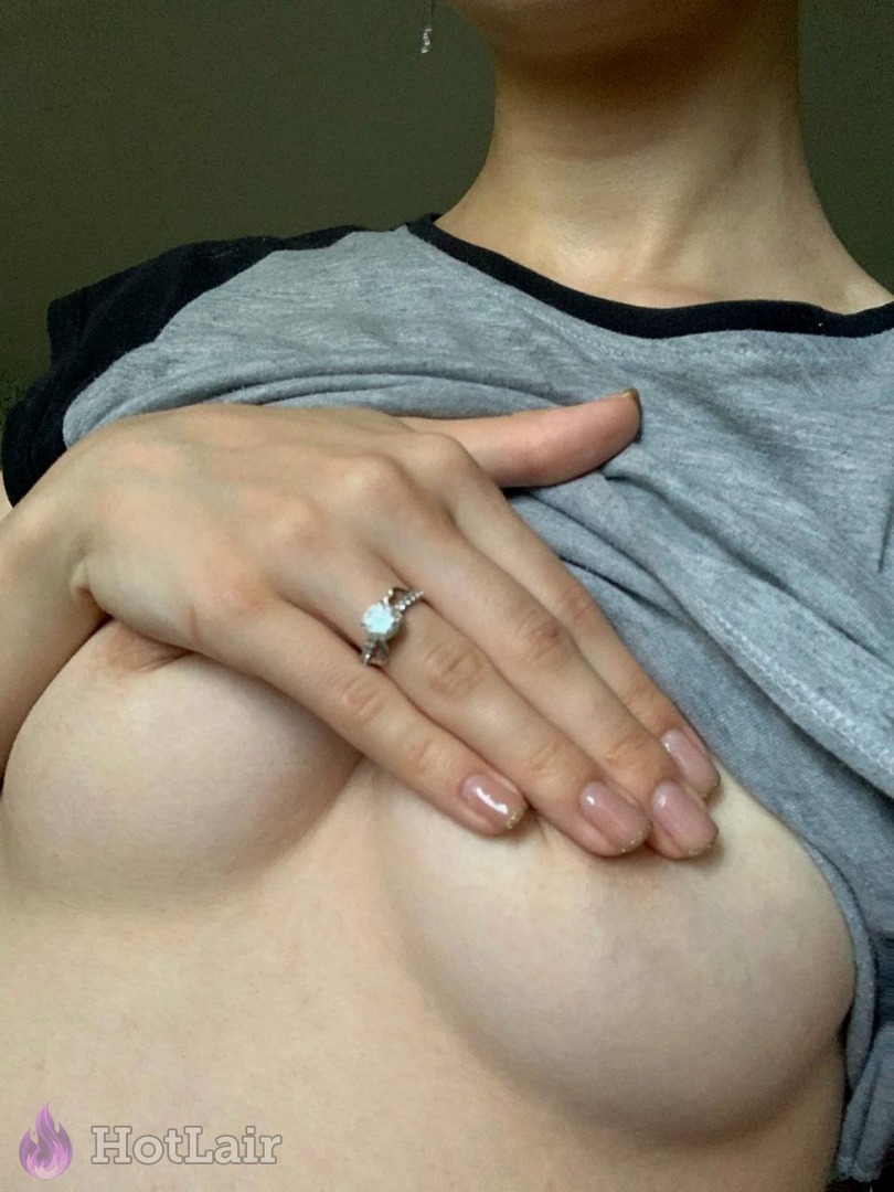 Primer plano de senos de mujer bajo camiseta gris siendo tocados por mano con anillo