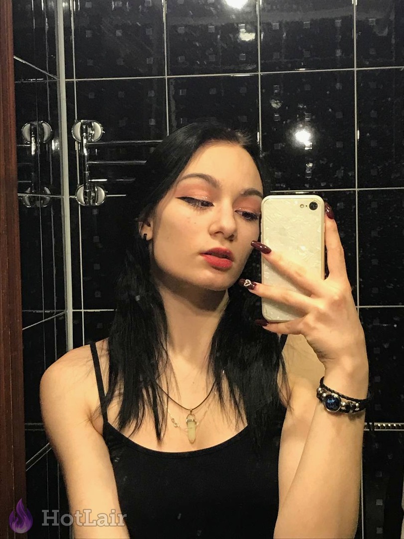 Brune prenant un selfie miroir dans une douche carrelée, en débardeur noir et maquillage prononcé