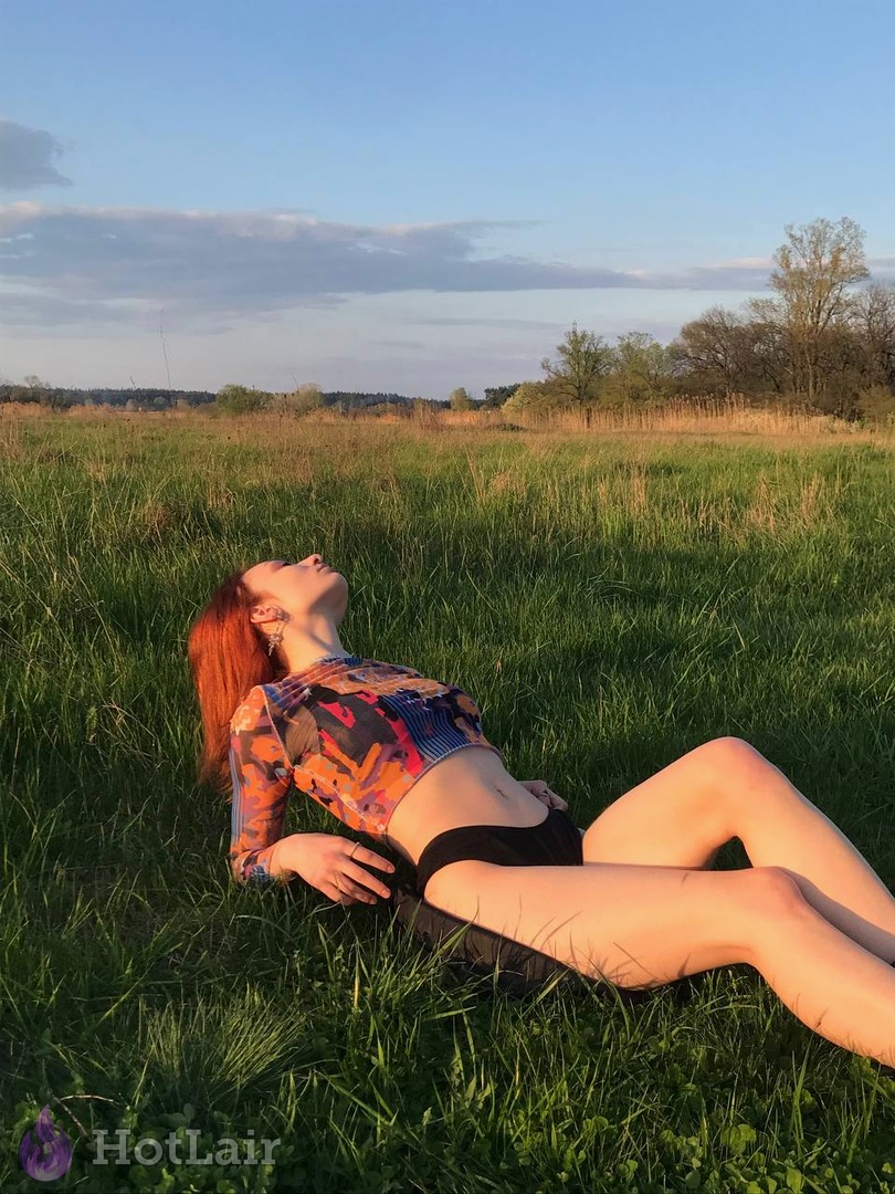 Rousse allongée dans l’herbe verte d’un champ au coucher de soleil, en crop top long coloré