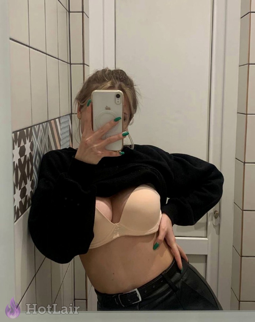 Femme en soutien-gorge push-up beige et pull noir se prenant en selfie miroir dans la salle de bain