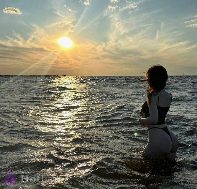 Mujer en bikini negro de pie en el mar al atardecer vista de espaldas con luz dorada