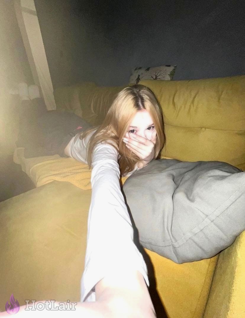 Rubia tumbada en sofá amarillo haciéndose selfie tapándose la boca con la mano