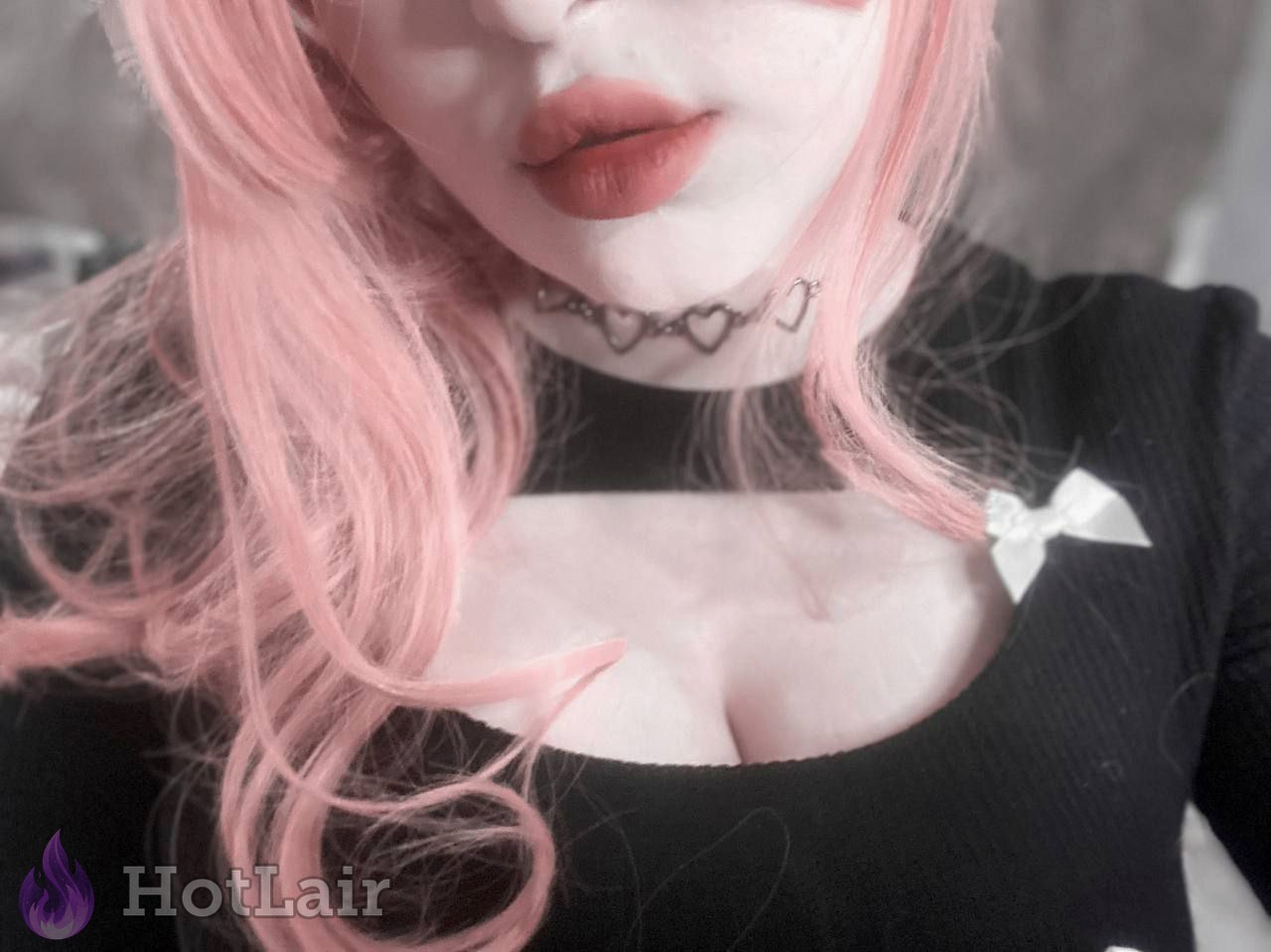 Primer plano de mujer con cabello rosa en top negro y collar con forma de corazón