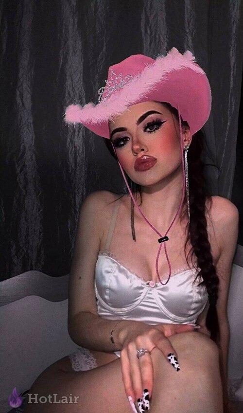 Mujer con sombrero vaquero rosa y lencería blanca de satén posando en la cama