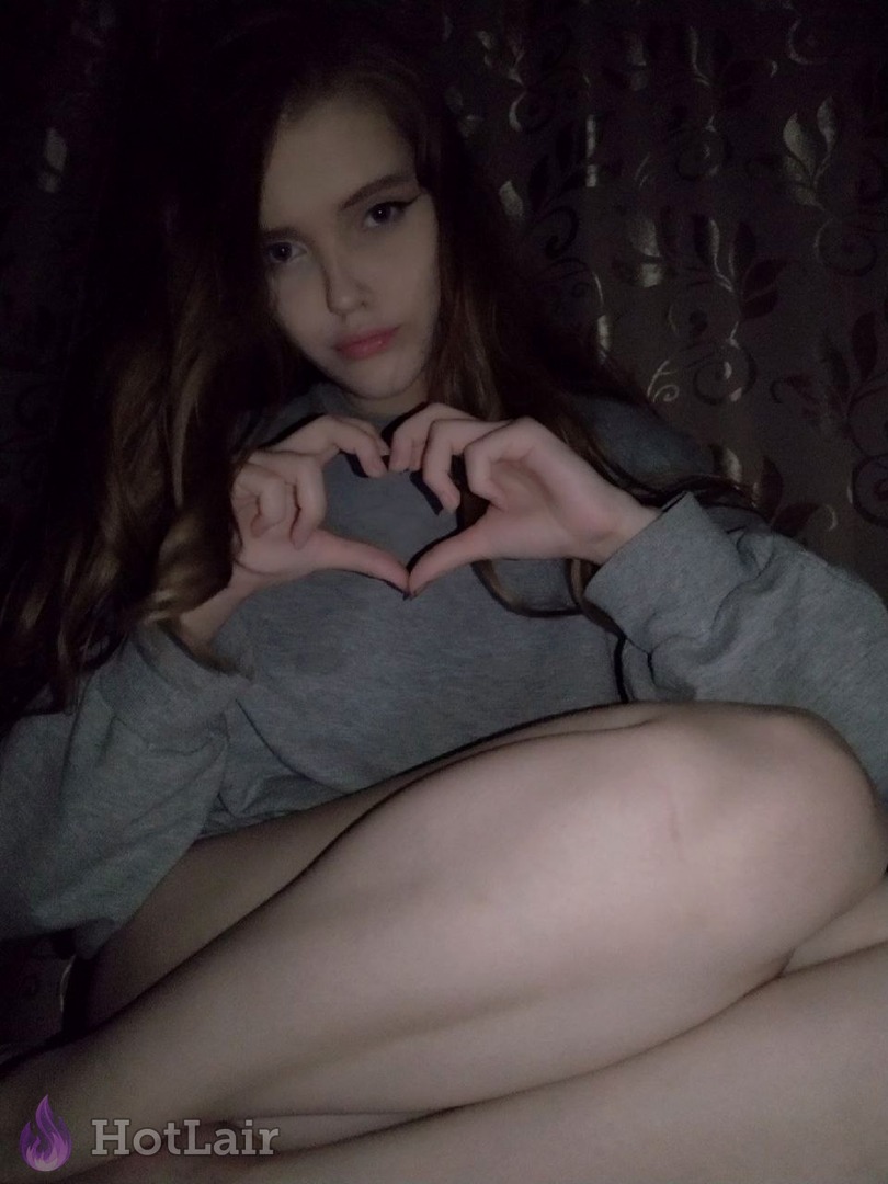 en suéter gris sentada formando un corazón con los dedos hacia la cámara