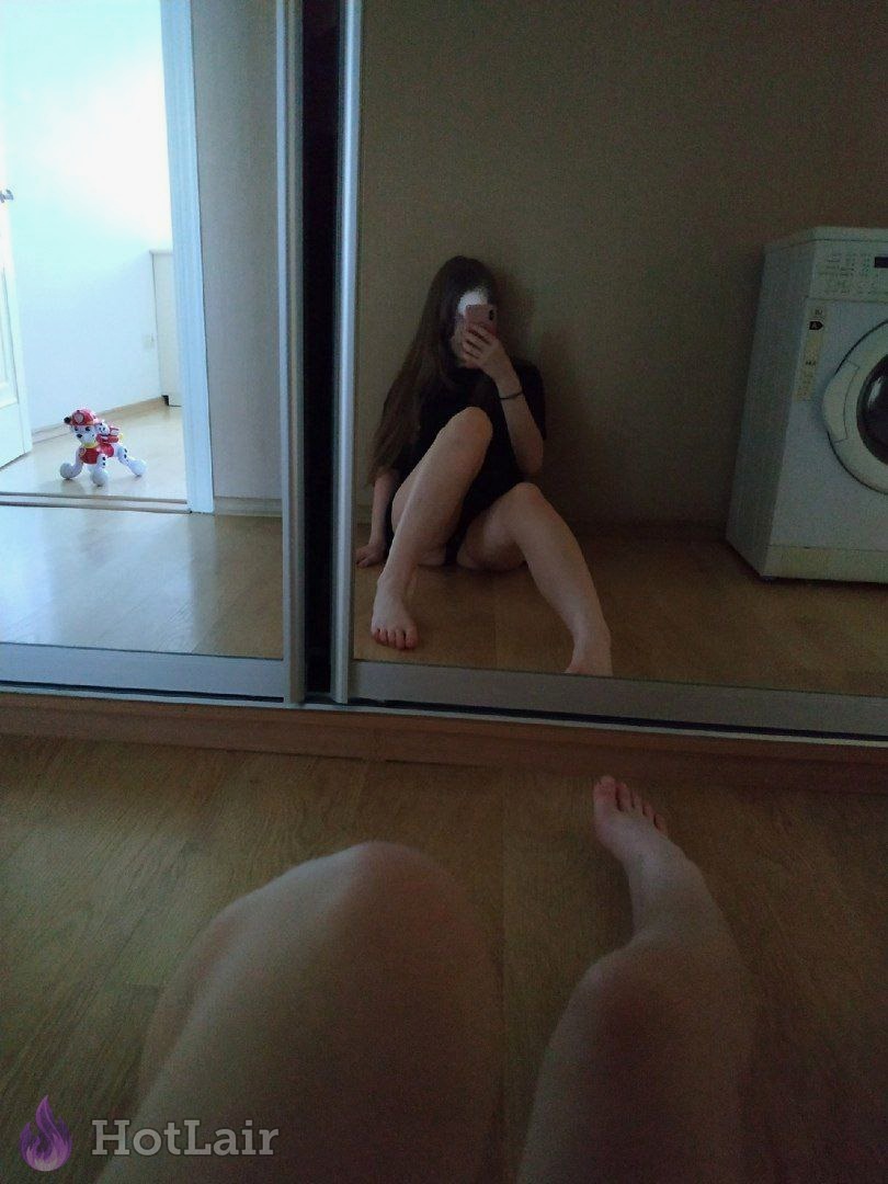 Selfie en espejo de en top negro sentada descalza en suelo de madera tomando foto con el teléfono