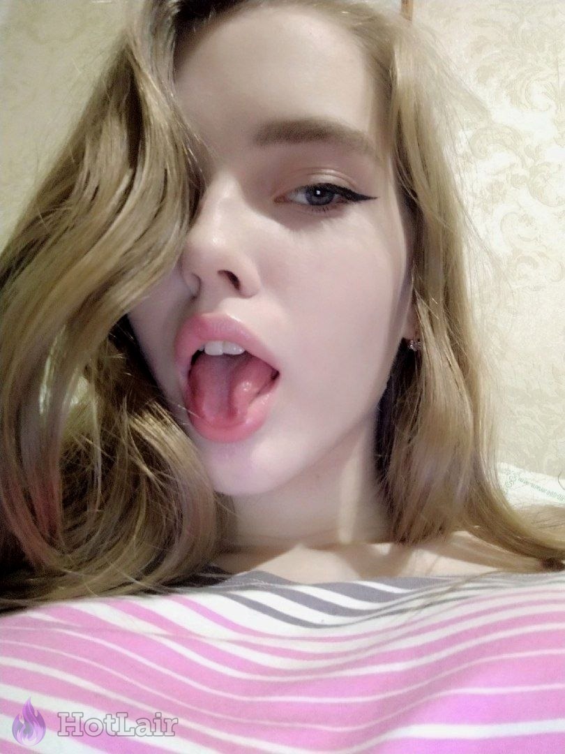 Selfie cercano de rubia con delineado alado, boca abierta y lengua fuera