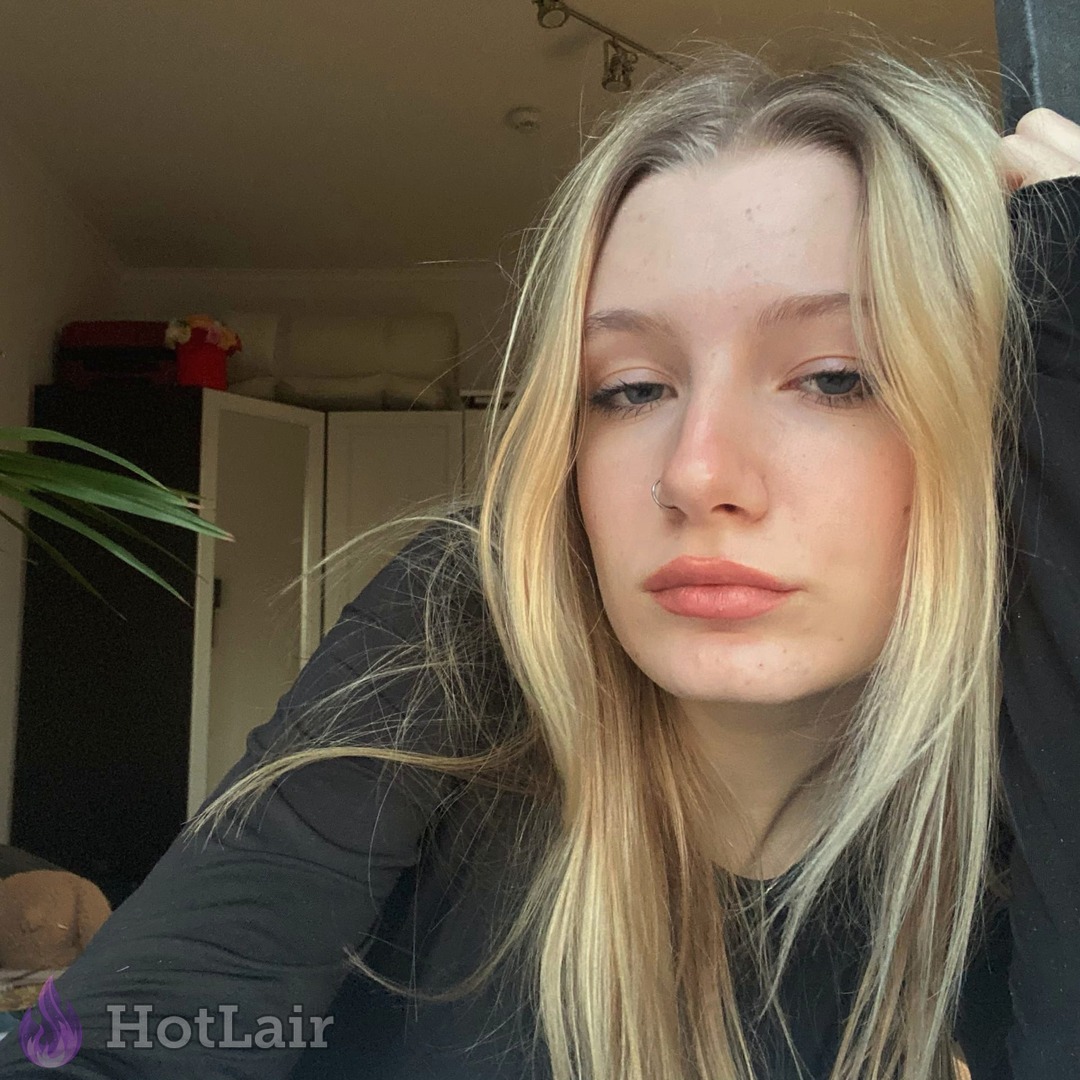 Selfie cercano de rubia con pelo largo en interior, mano en el cabello mirando a la cámara