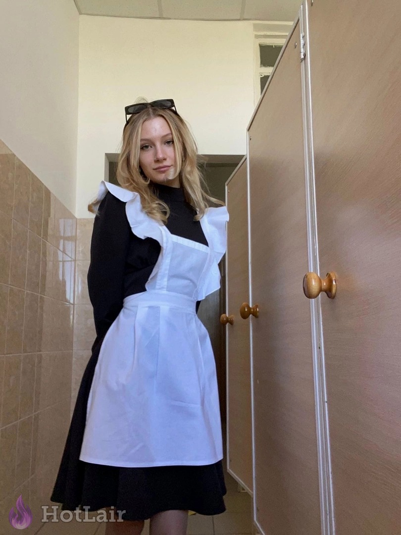 rubia de pie en el pasillo con vestido negro y gran delantal blanco de doncella, gafas en la cabeza