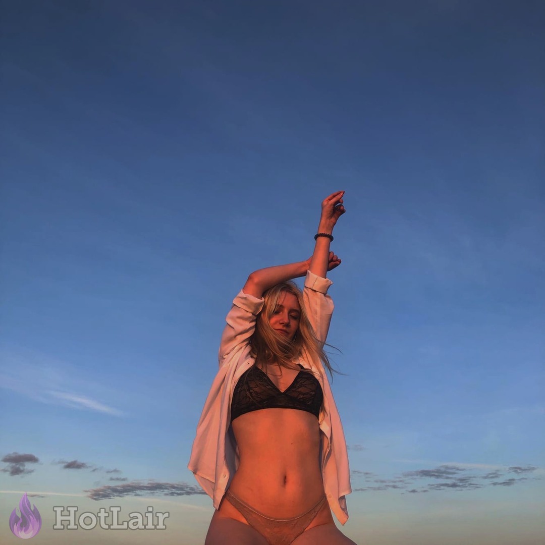 Rubia posando sensualmente al atardecer contra el cielo azul con camisa blanca abierta sobre lencería de encaje negro