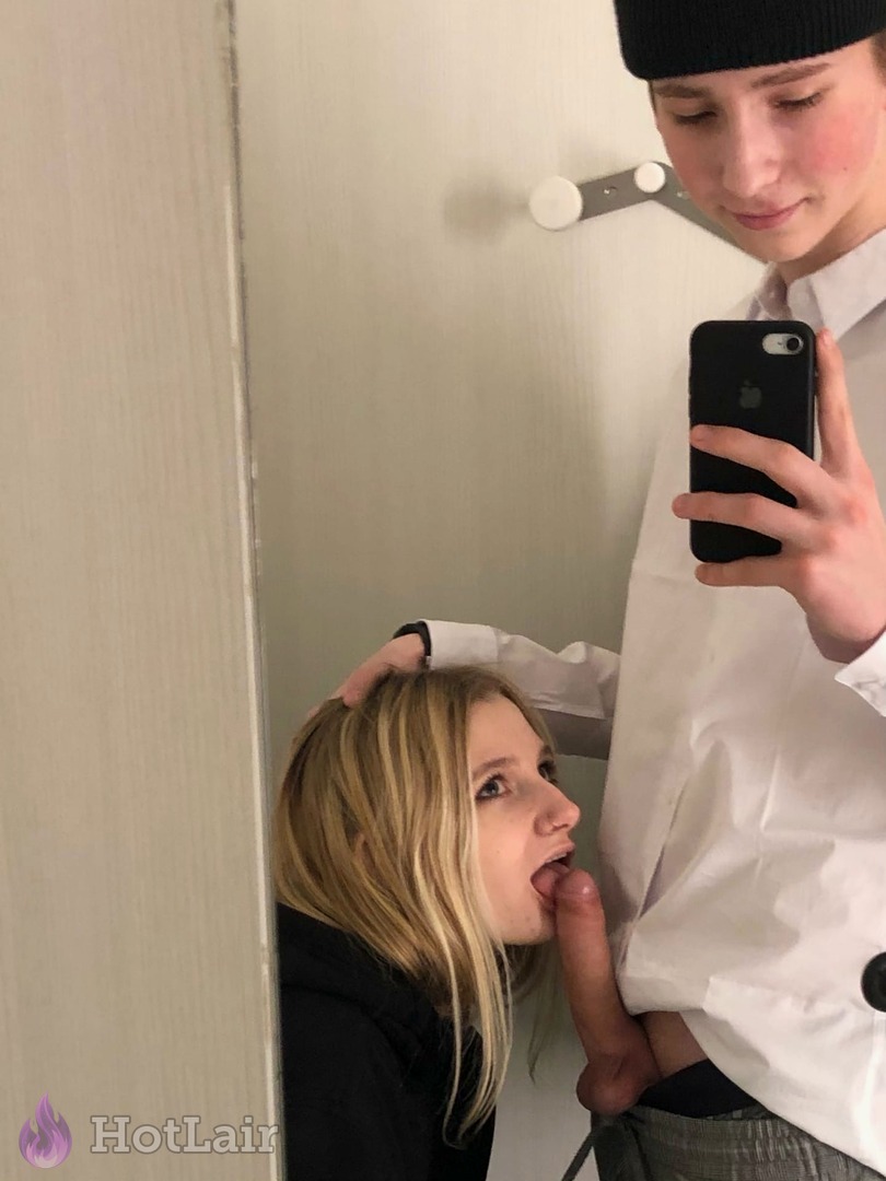 rubia de rodillas practicando sexo oral a un hombre con gorro que se hace selfie en el espejo