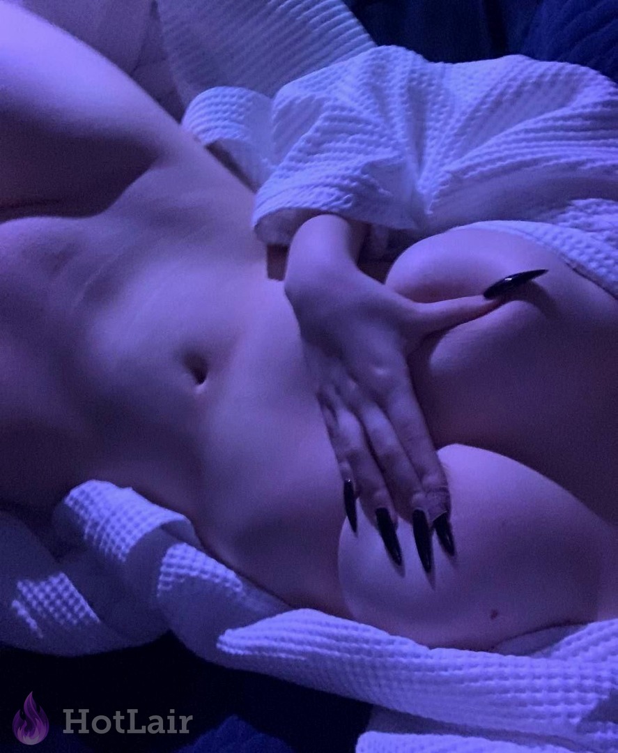 Mujer desnuda acostada sobre bata blanca bajo luz púrpura, uñas largas negras en el cuerpo