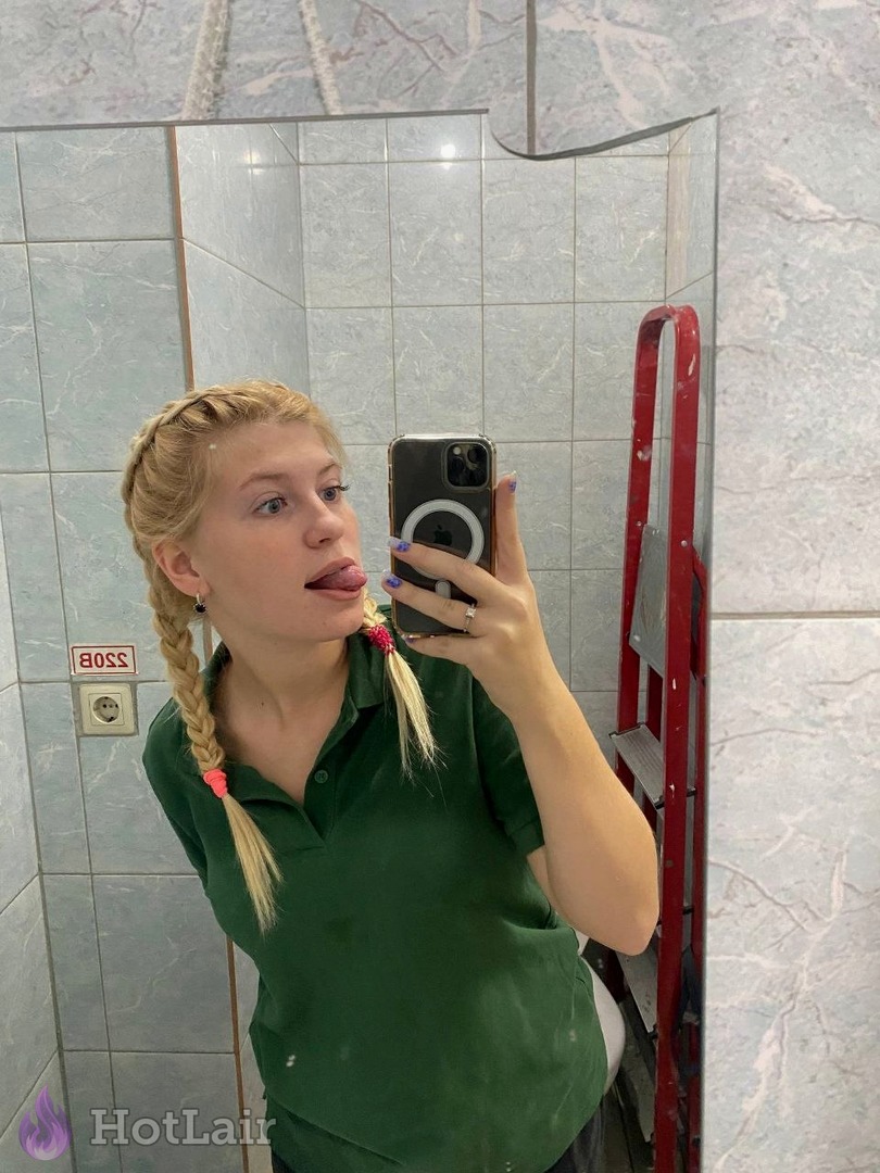 Rubia con trenzas haciendo un selfie en el espejo en el baño con polo verde