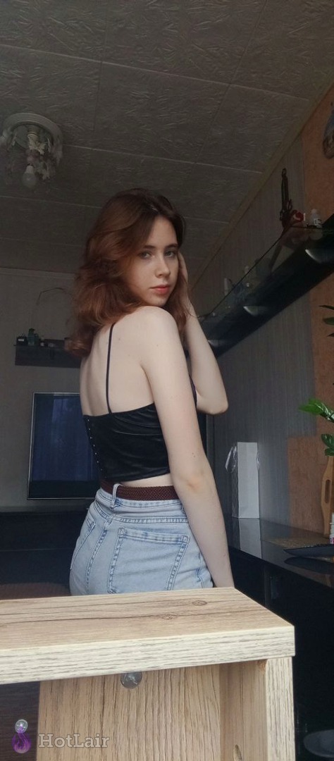 Morena con top de terciopelo negro y jeans de pie en interior mirando por encima del hombro