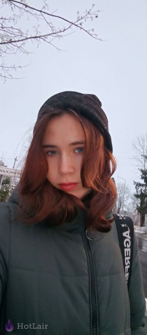 Mujer pelirroja con chaqueta verde y gorro negro haciéndose un selfie al aire libre