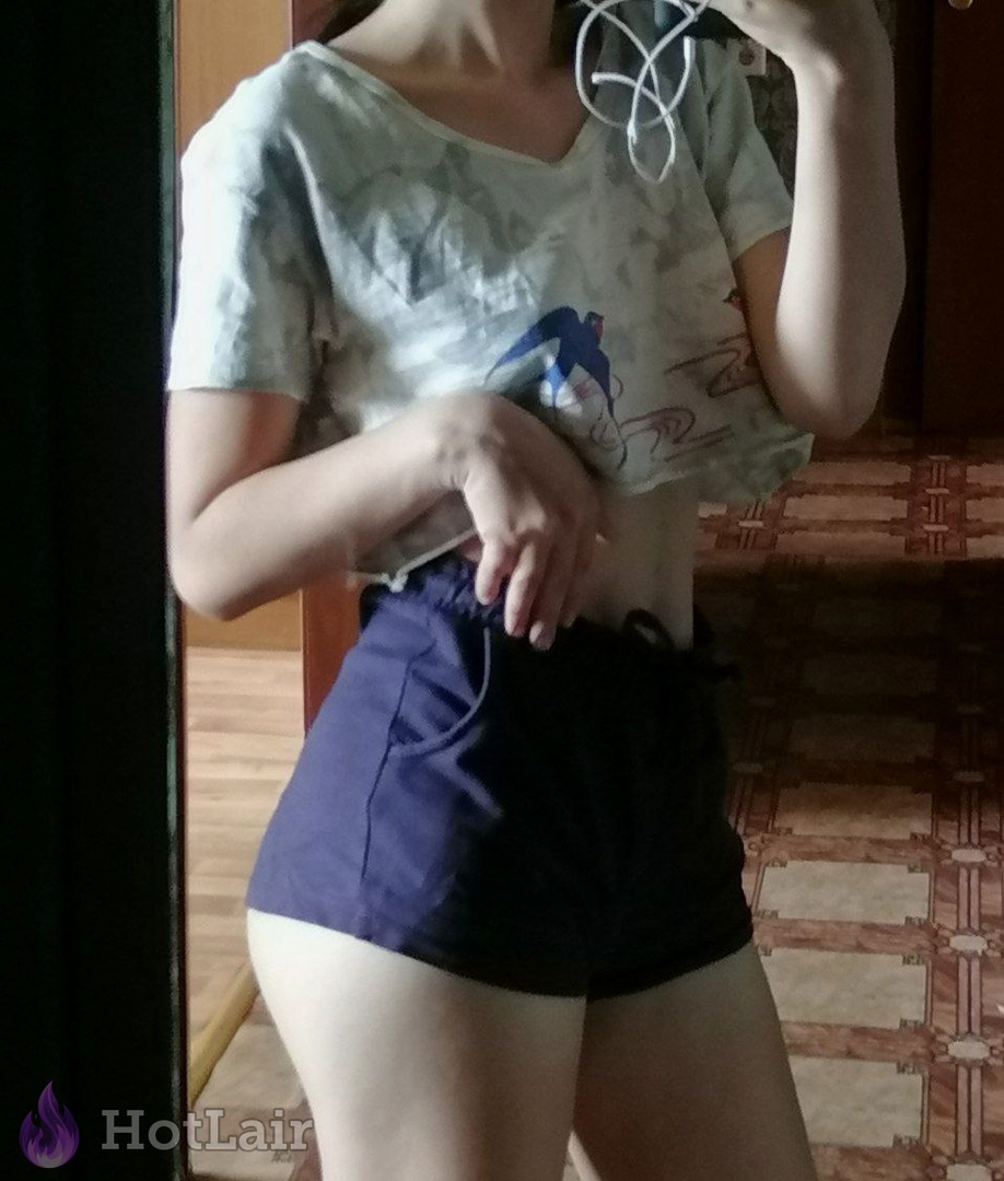 Mujer con crop top camuflado y shorts oscuros haciéndose un selfie en el espejo