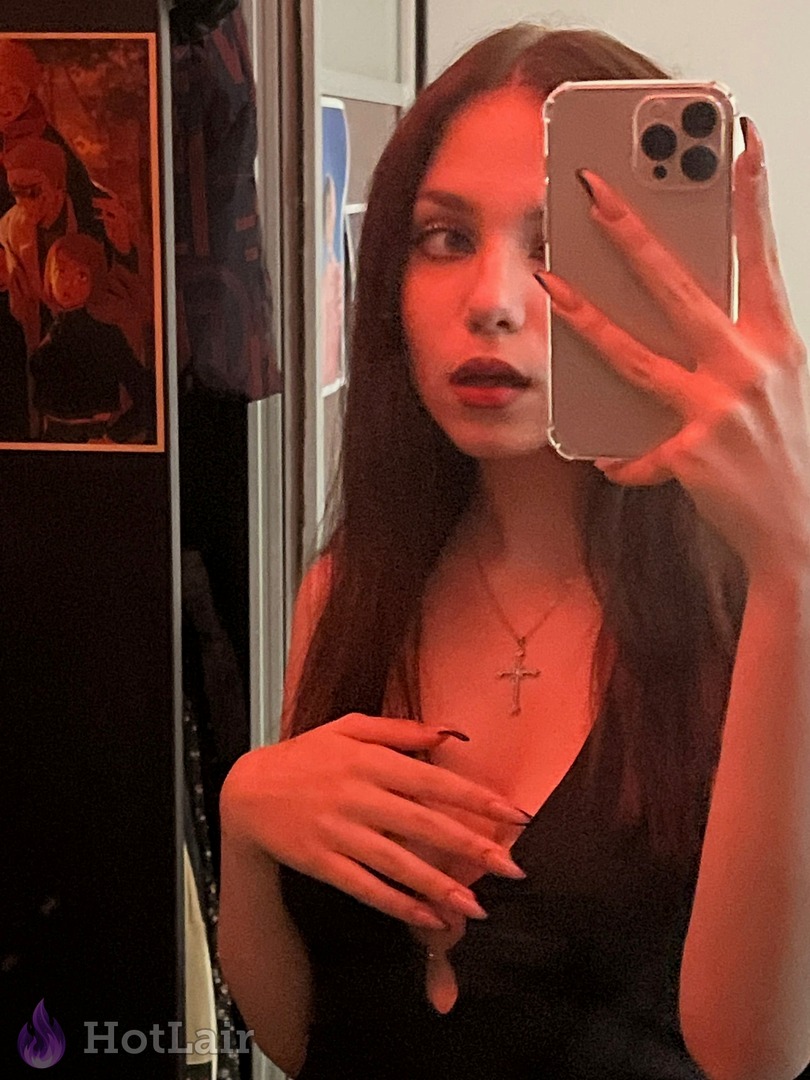 de largo cabello oscuro en vestido negro haciéndose un selfie en el espejo con luz roja