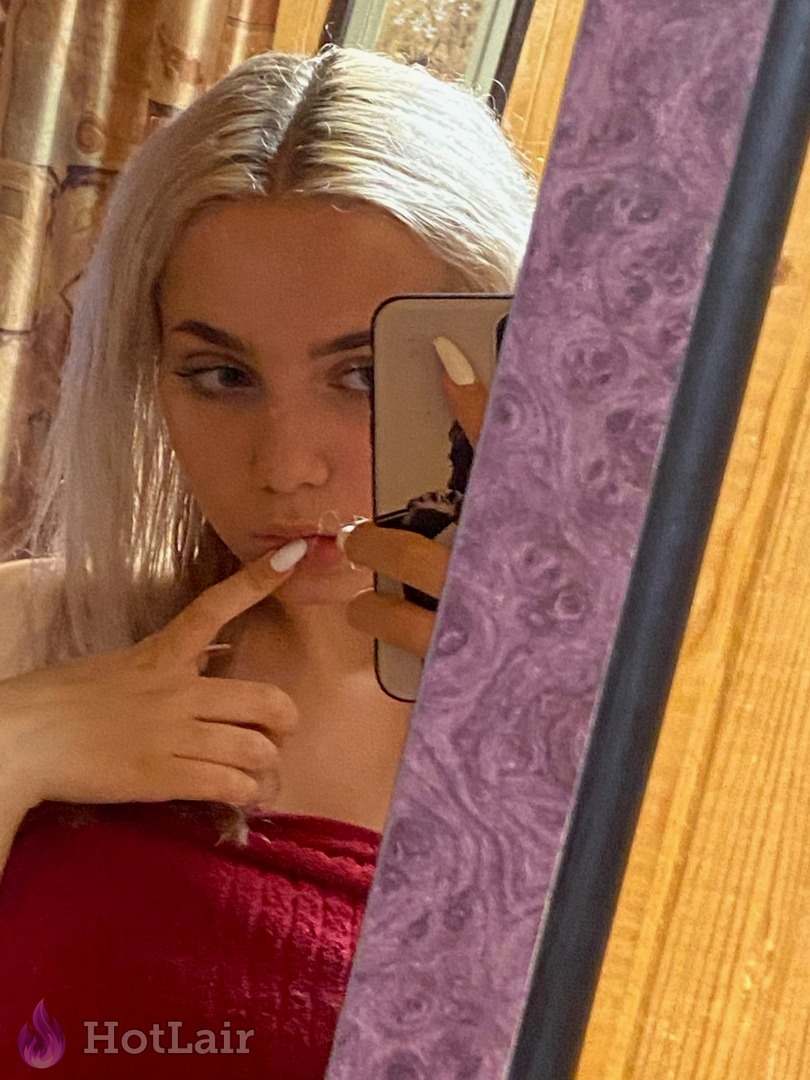 Rubia en top rojo haciéndose un selfie en el espejo, tocándose los labios con el dedo
