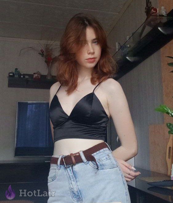 con cabello castaño rojizo en top negro de satén y jeans azules posando en interiores
